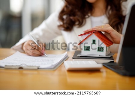Close up of woman hands holding home model, Real estate brokerage contracts for sale and rent with insurance loan mortgage concepts.
