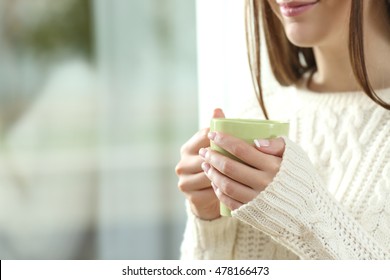 Close up of a woman hands holding a hot coffee cup in winter near a window at home with outdoors in the background