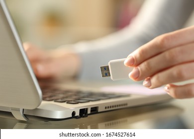 Close up of woman hands holding usb flash drive next to laptop on a desk at home