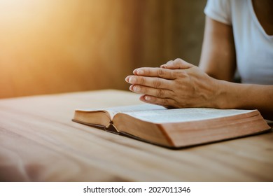 Close up of a woman hands praying on an open bible on a wooden table with window light Bokeh, Christian praise and worship, devotional concept background with copy space. Jesus Christ's disciples life