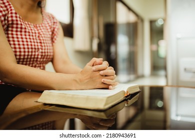Close up of a woman hands praying on the open holy bible on a table indoor with the windows light lay warm tone . Christian faith and trust concept with copy space. Christian devotional background