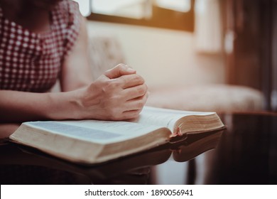 Close up of woman hands prays over open bible on table in home with window light, copy space