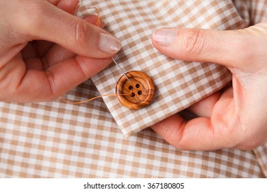 Close Up Of Woman Hands Sewing Button On Brown Fabric