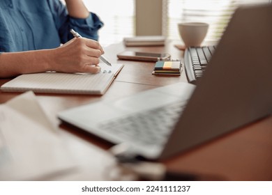 Close up of woman hands taking notes while working in cozy home office remotely - Powered by Shutterstock