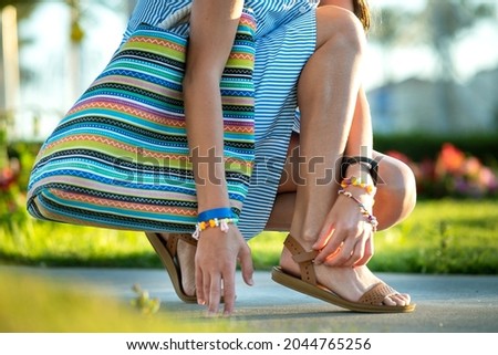 Close up of woman hands tying her open summer sandals shoes on sidewalk in sunny weather.