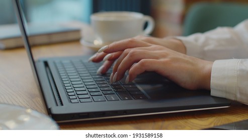 Close up of woman hands typing on laptop. Woman working on laptop while sitting at table in cozy cafe.