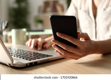 Close up of woman hands using laptop checking smart phone at night at home - Powered by Shutterstock