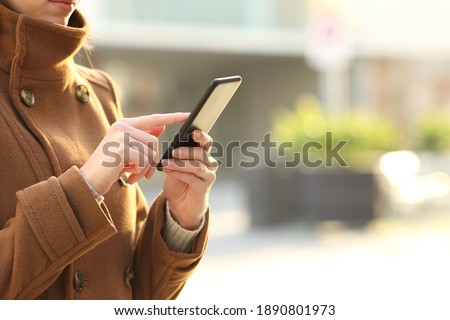Close up of woman hands in winter using smart phone walking in the street