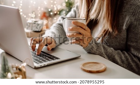 Close up of woman hands with, gifts, coffee cup and laptop. Online shopping at Christmas holidays. Freelance girl woking from home office. Female typing at notebook computer. Christmas moments.