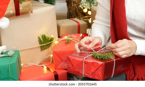 Close Up Woman Hands Wrap Present Gift In Cozy Living Room. Woman Wrapping Christmas Gift Box Under Xmas Tree. Asian Woman Decor Bauble Ball Christmas Tree In Xmas Holiday Winter Seasonal Celebration