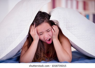 Close up of woman with her head under her pillow trying to sleep at night and yawning, insomnia concept - Shutterstock ID 1018735015