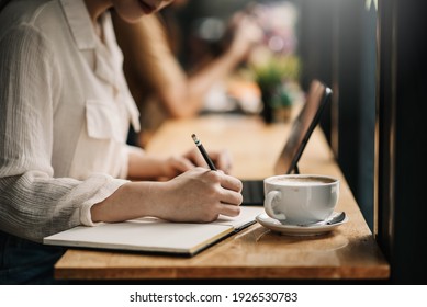 Close up of a woman hold a pencil taking notes and drinking coffee at the café. - Powered by Shutterstock