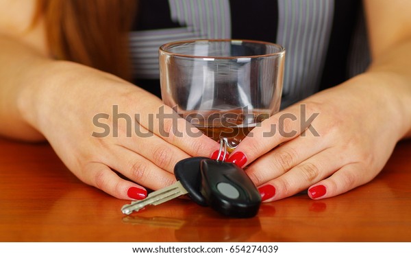 Close up of a woman holding\
with both hands a glass of whiskey and car keys, over a wooden\
table