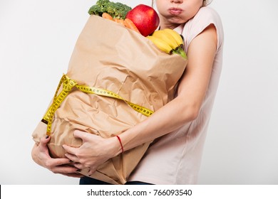 Close Up Of A Woman Holding Heavy Bag With Groceries Wrapped With A Measuring Tape Isolated Over White Background