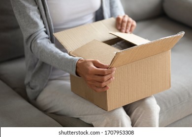 Close up woman holding parcel in hands, unpacking, curious young female opening cardboard box, gift, sitting on couch at home, client customer received online store order, delivery service - Shutterstock ID 1707953308