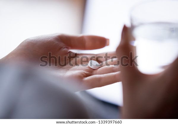 Close up woman holding pill in hand with water.\
Female going to take tablet from headache, painkiller, medication\
drinking clear water from glass. Healthcare, medicine, treatment,\
therapy concept