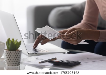 Close up woman holding receipt, using laptop, calculating bills, money, sitting at table on couch, female planning budget, managing expenses, finances, checking internet banking service