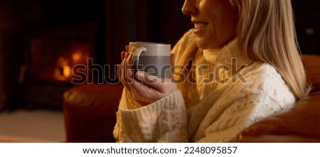 Close Up Of Woman At Home In Lounge With Cosy Fire With Hot Drink
