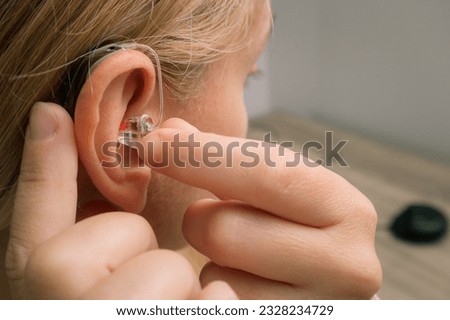 Close up of Woman inserting her hearing aid into ear. Blonde Woman with Modern Hearing Aid. Hearing Impaired.