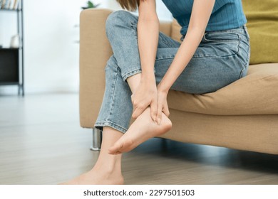 Close up woman leg knee pain feet. Female pain with ankle because walk too much. Massaging suffering knee foot. Pain at calves sitting on couch at home. Hands massage legs on sofa.