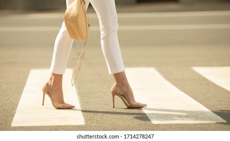 Close Up Of Woman Legs Walking On Crosswalk. The Woman Is Wearing Shoes On High Heels.