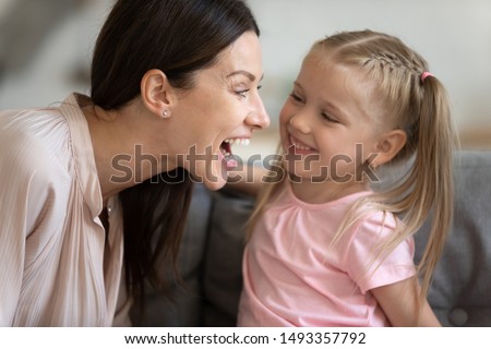 Close up woman and little girl having fun play sit on couch, mother clearly says words that daughter repeats them develop her language skills, correction of speech or just fool around at home concept