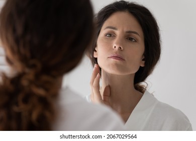 Close up woman looks in mirror touch face feels upset detects mimic wrinkles or pigment spots due ageing process, need facial massage, cosmetics or treatment prevent age-related skin changes concept