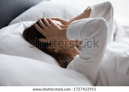 Close up woman lying in bed woke up in early morning touch head with palms feels tired not enough of rest, insomnia sleep disorder anxious by personal problems, unhealthy migraine and headache concept