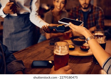 Close up of woman making contactless payment with cell phone in a pub. - Powered by Shutterstock