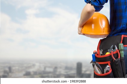 Close Up Of Woman Mechanic With Yellow Helmet In Hand Against City Background