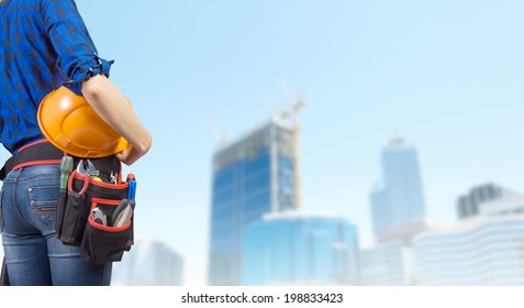 Close Up Of Woman Mechanic With Yellow Helmet In Hand Against City Background