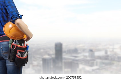 Close Up Of Woman Mechanic With Yellow Helmet In Hand Against City Background