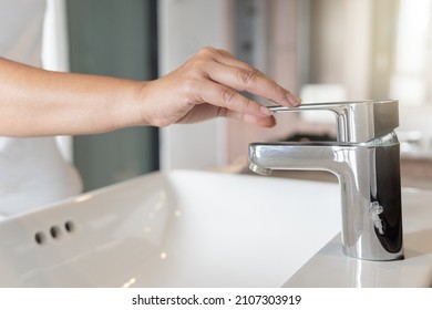 Close up Woman open chrome faucet washbasin to washing hands rubbing with soap for corona virus at water tap. Faucet and water drop off. Bathroom interior background with sink basin and water tap. - Shutterstock ID 2107303919