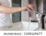 close up Woman open pull chrome faucet washbasin to washing hand soap for corona virus at water tap. push off water running drop off. Bathroom interior background with sink basin faucet tap.