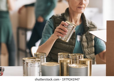 Close up of woman packing canned food to boxes at charity and donations event, copy space