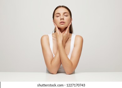 Close Up Of Woman With Perfect Healthy Fresh Skin Sits At The Table, Hands Crossed And Touching Face,happy With The Effect Of The Mask, Eyes Closed In Pleasure, Hair Pulled Back, Over White Background