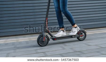 Close up of woman riding black electric kick scooter at cityscape, motion blur