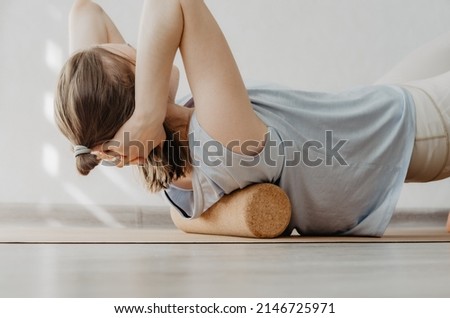 Close up of woman rolling back on a cork massage roller to release tension in back muscles. Concept: self care practices at home, sustainable props, physical health