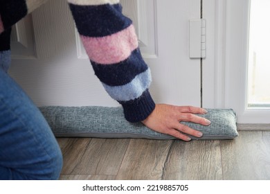 Close Up Of Woman Saving Enegy Insulating Home Putting Draught Excluder Against Front Door