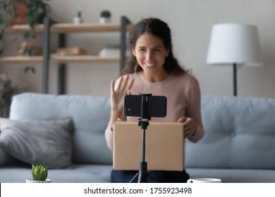 Close up woman shooting unboxing video on smartphone, unpacking parcel with internet store order, girl vlogger recording vlog, talking, waving hand, saying hello, sitting on couch at home
