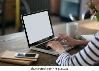 Close up of a woman sitting in front of her portable computer empty screen with coffee, phone at table and hands at keyboard in the room. Distance learning or work from home concept. Laptop mockup