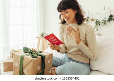 Close Up Of Woman Sitting On Bed With Christmas Present. Smiling Woman Holding A Christmas Card.