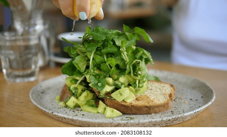 Close up of a woman squeezing lemon on the avocado toast with green leaves in the cafe on healthy breakfast  - Powered by Shutterstock