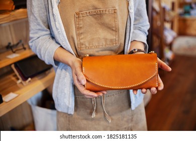 Close up of woman standing in a leather shop, holding tan leather clutch bag. - Powered by Shutterstock