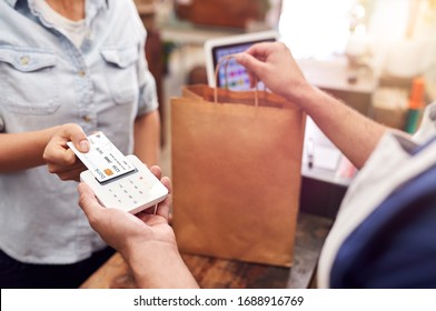 Close Up Of Woman In Store Making Contactless Payment At Sales Desk Holding Credit Card To Reader