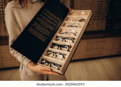 Close up of woman taking eyeglasses from rack. Female choosing stylish prescription glasses on eyewear display stand in optical store. Vision health, blindness concept. Selective focus.  - Powered by Shutterstock