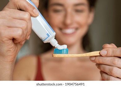 Cierre de la mujer con cepillo dental aplicando pasta en el baño. Cierre de las manos de una niña exprimiendo pasta de dientes sobre un cepillo de madera ecológico. Mujer sonriente aplicando pasta dental en cepillo de dientes ecológico.