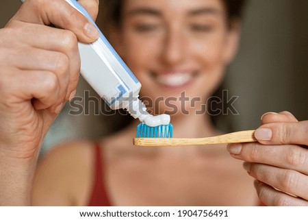 Close up of woman with tooth brush applying paste in bathroom. Closeup of girl hands squeezing toothpaste on ecological wooden brush. Smiling woman applying toothpaste on eco friendly toothbrush.