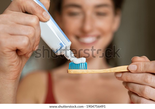Close up of woman with tooth brush applying\
paste in bathroom. Closeup of girl hands squeezing toothpaste on\
ecological wooden brush. Smiling woman applying toothpaste on eco\
friendly toothbrush.