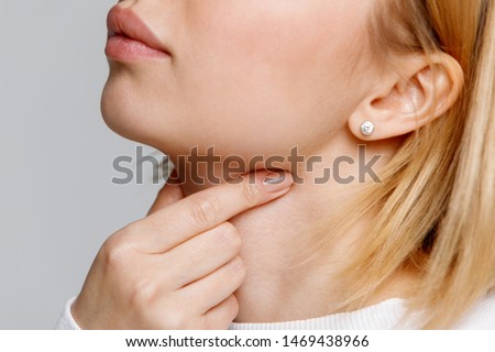 Close up of woman touches fingers of sore throat, isolated on gray background. Thyroid gland, painful swallowing, tonsillitis, laryngeal swelling concept. Inflammation of the upper respiratory tract